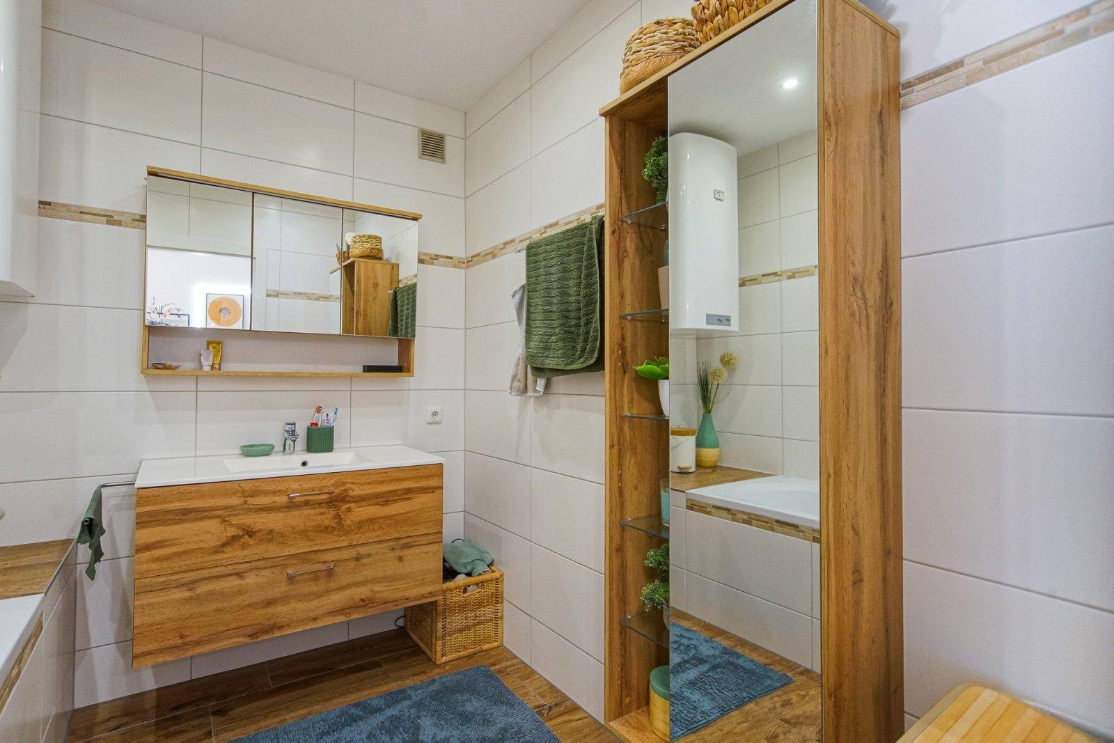 Modernes Badezimmer mit Badewanne, Holzwaschtisch und hohem Spiegelschrank für zusätzlichen Stauraum.