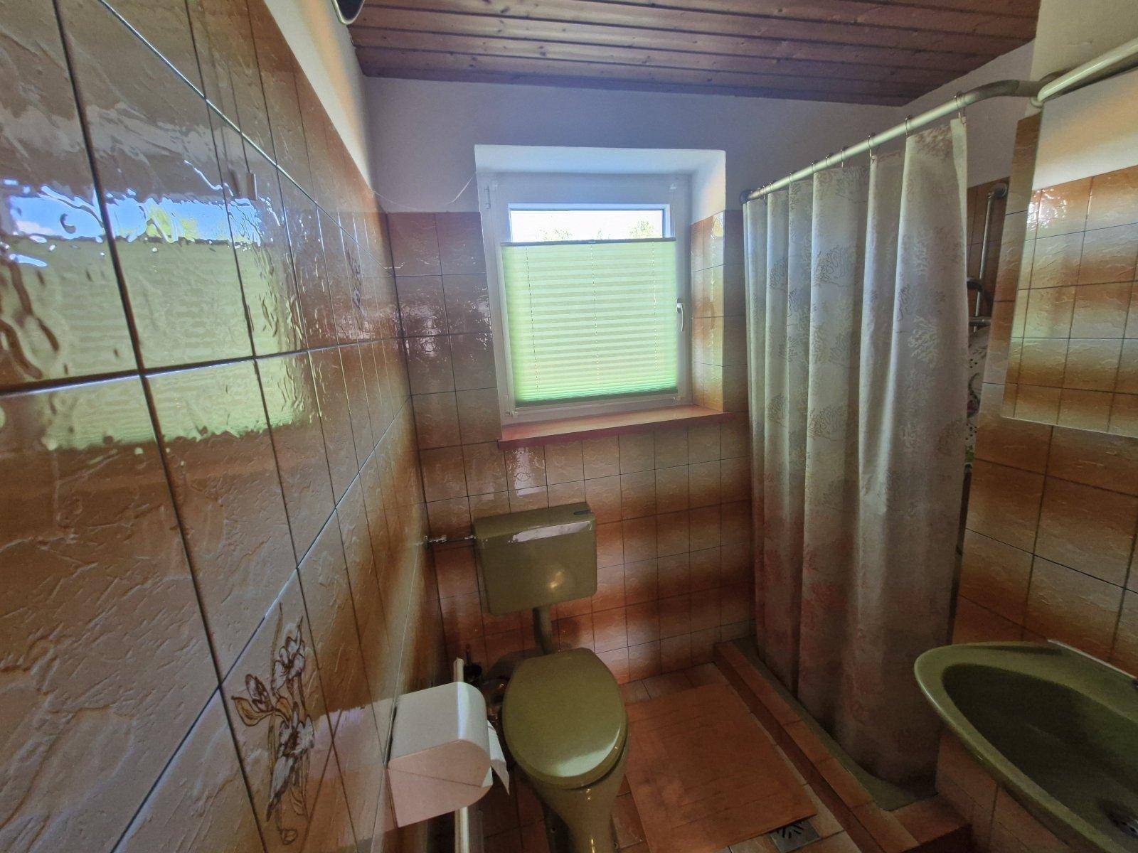 Badezimmer mit braunen Fliesen, WC, Dusche und Holzdecke im rustikalen Stil.