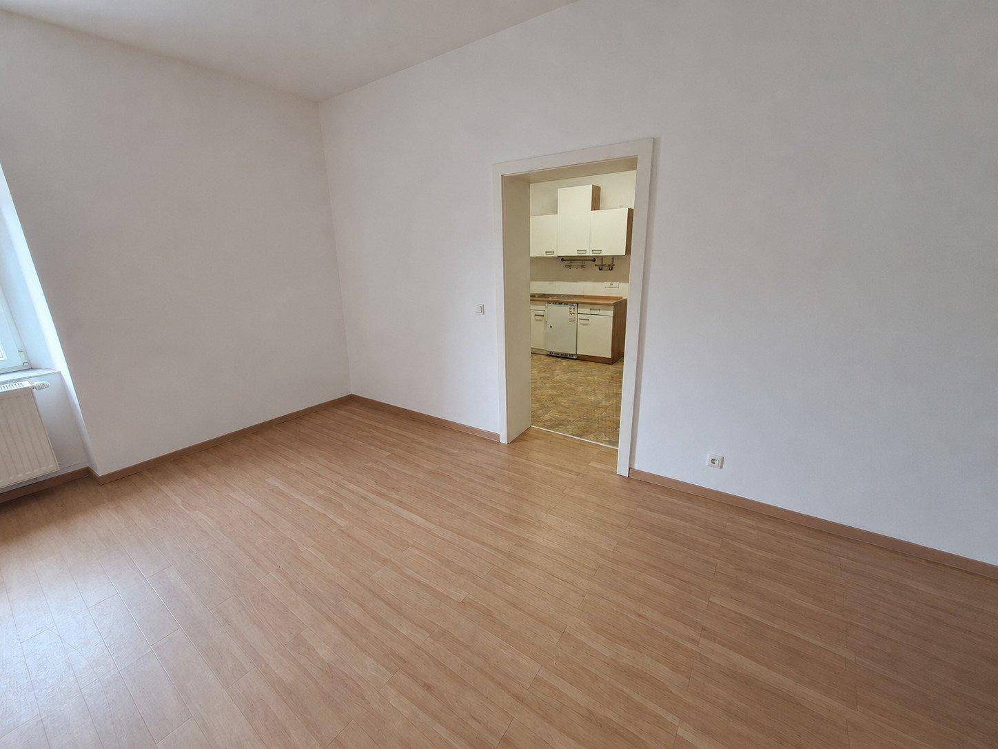 Geräumiger Wohnbereich mit Laminatboden und Durchgang zu einer separaten Küche.