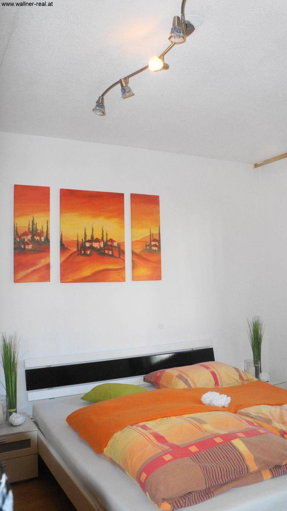 Schlafzimmer mit Doppelbett, weißen Wänden und farbenfroher Wanddekoration.