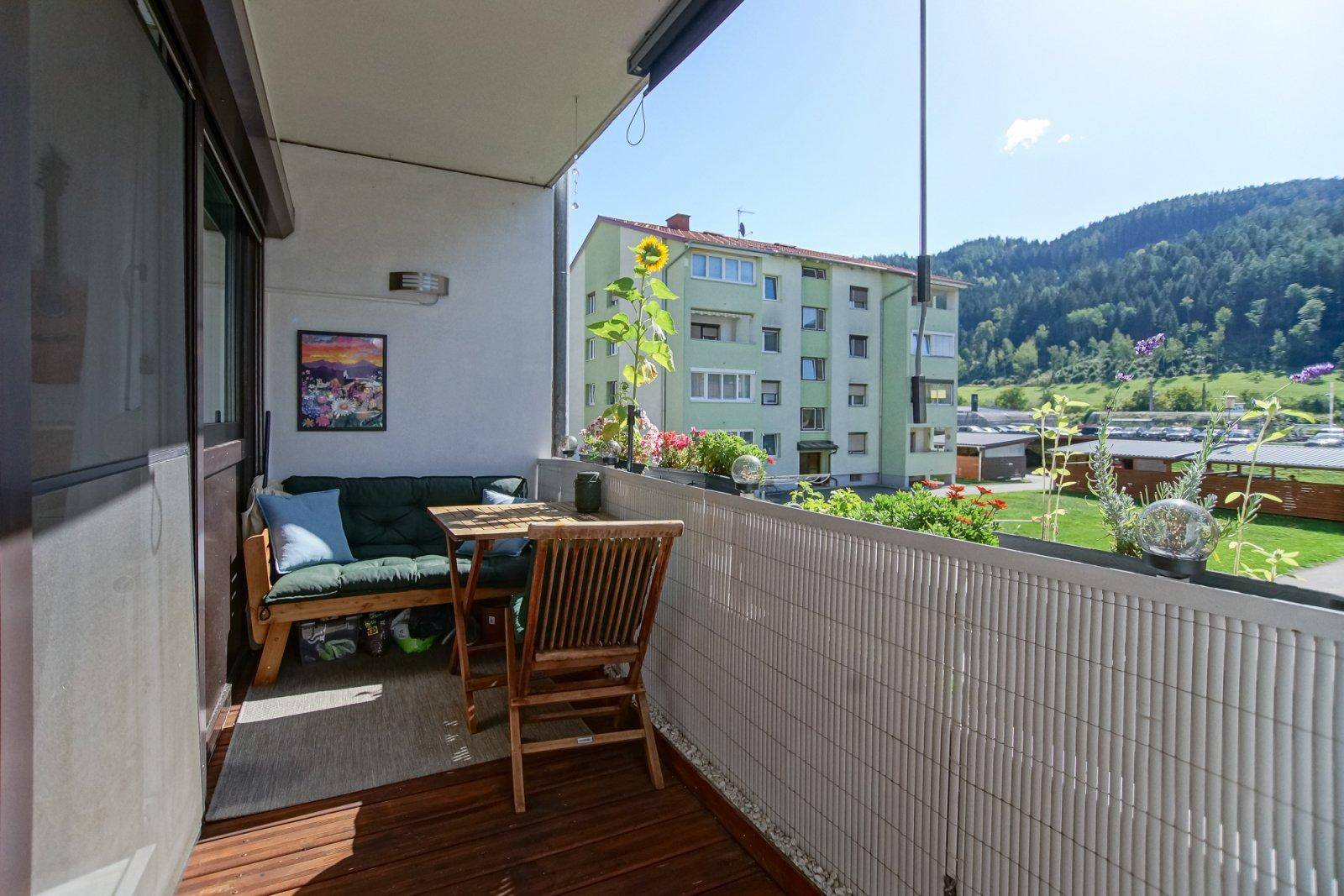 Heller Balkon mit Holzfußboden, Sitzgelegenheiten und Blick auf die Umgebung und grüne Hügel.