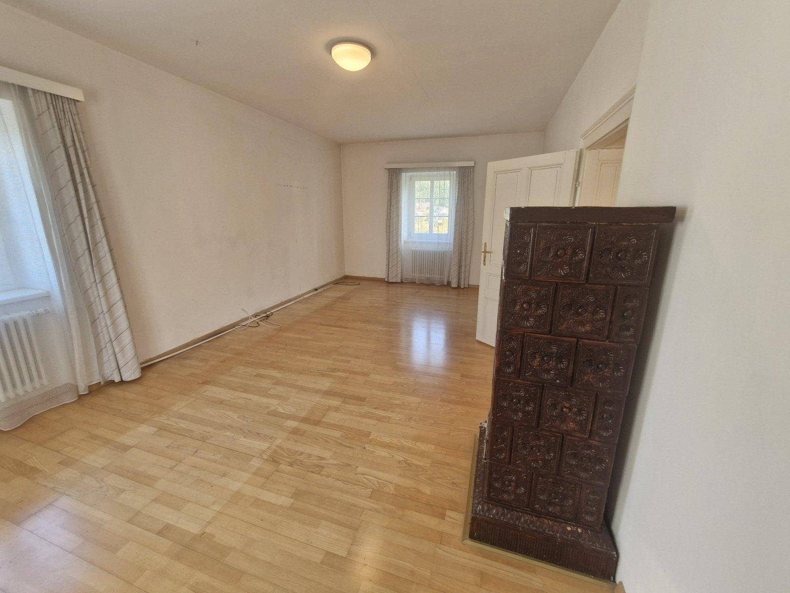 Helles Zimmer mit Parkettboden und einem traditionellen Kachelofen, ideal als Wohn- oder Schlafzimmer.