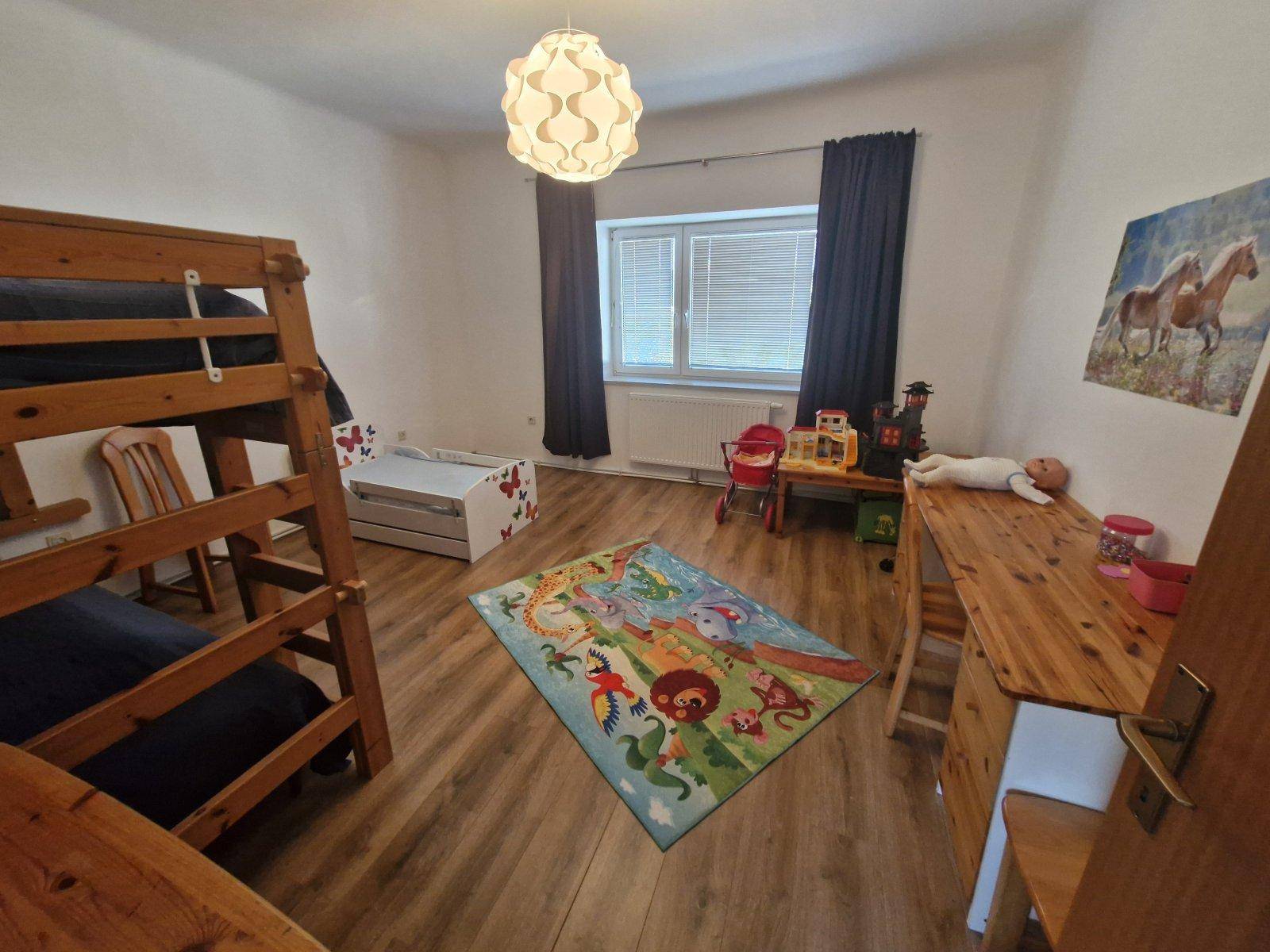 Helles Kinderzimmer mit Etagenbett, Holzmöbeln und farbenfrohem Teppich, ideal für junge Familien.