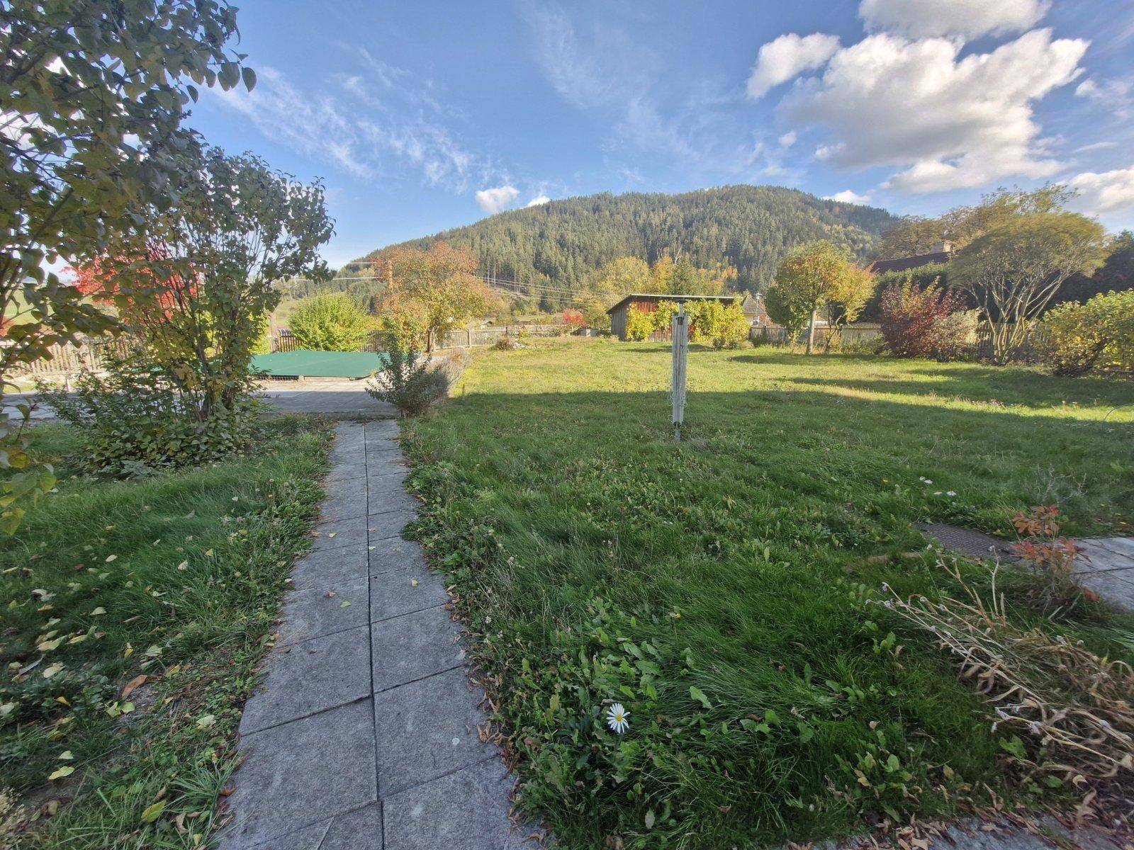 Gepflasterter Weg durch die Rasenfläche des Gartens mit Blick auf die bewaldeten Hügel.