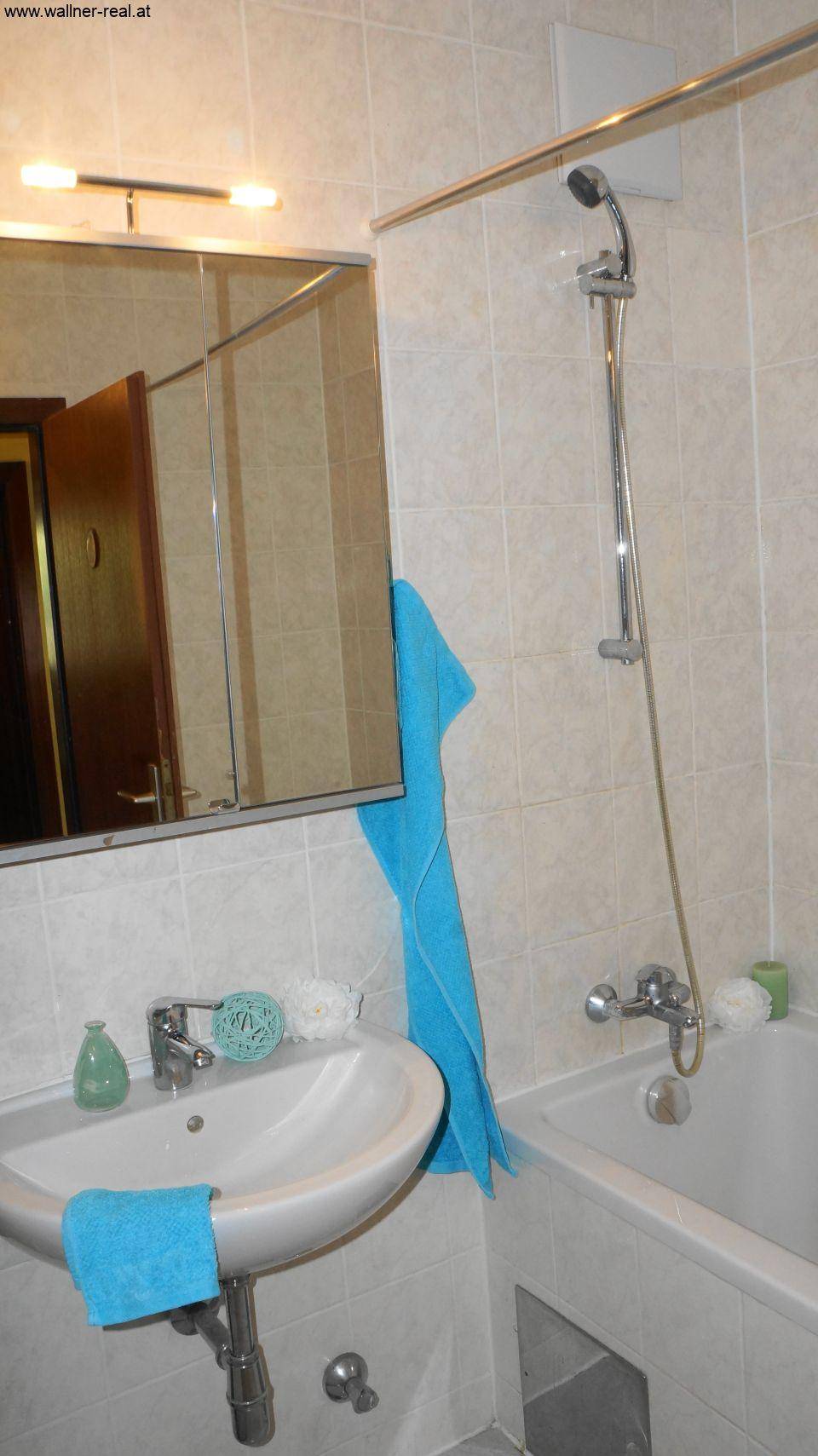 Helles Badezimmer mit Badewanne, Duschvorrichtung und Spiegelschrank über dem Waschbecken.