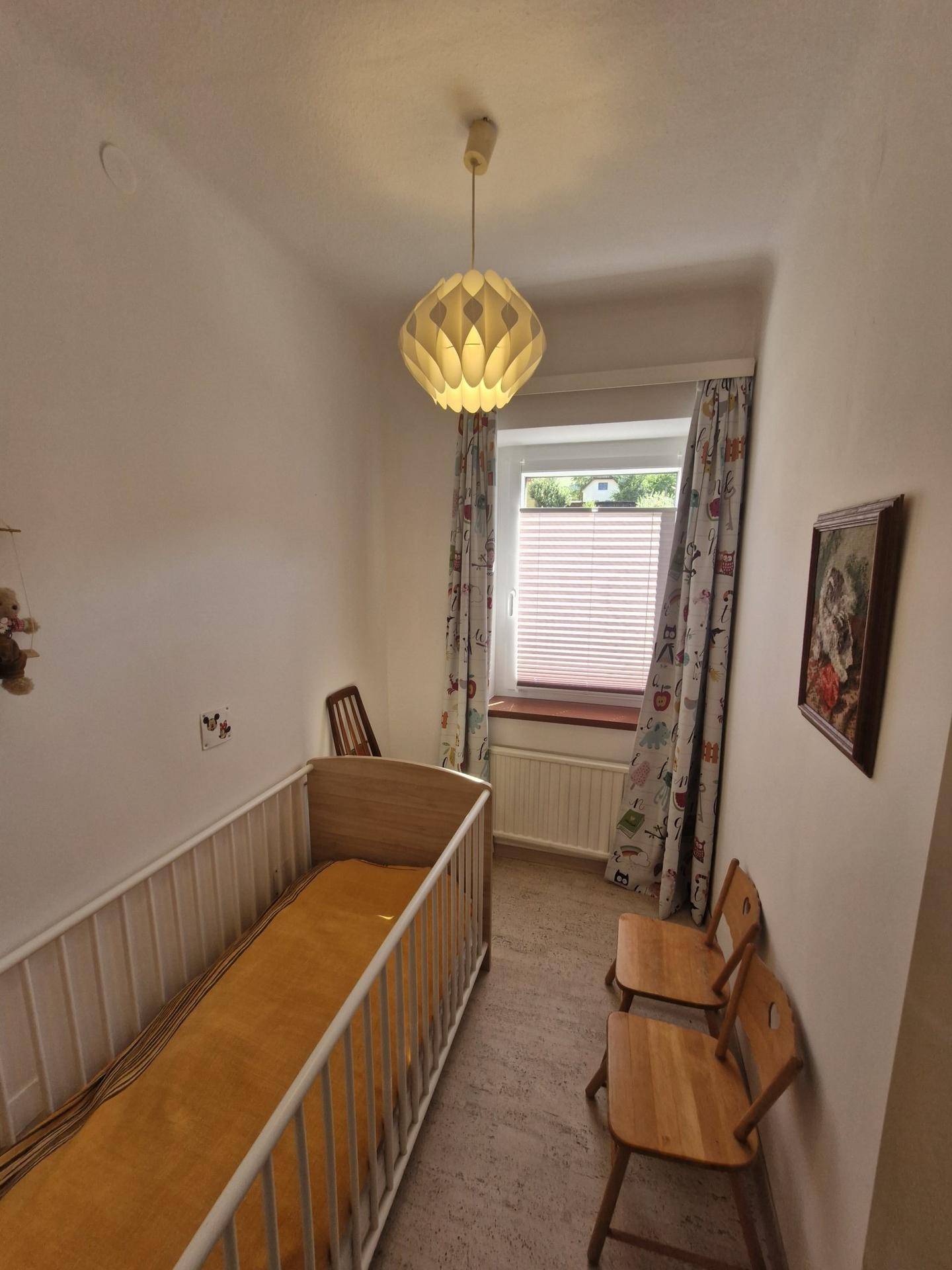 Kinderzimmer mit Babybett, Holzstühlen und Fenster mit Jalousien für viel Licht.