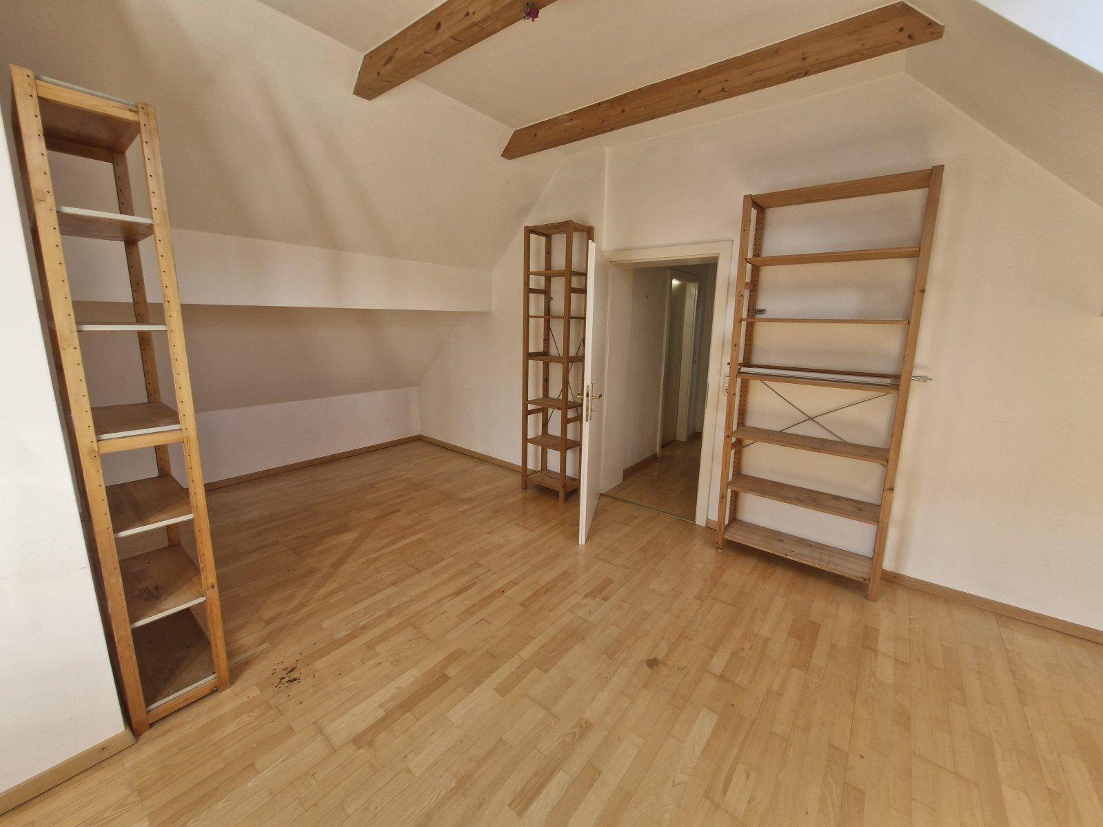 Dachgeschossraum mit Holzbalken und Parkettboden, ausgestattet mit mehreren Holzregalen.