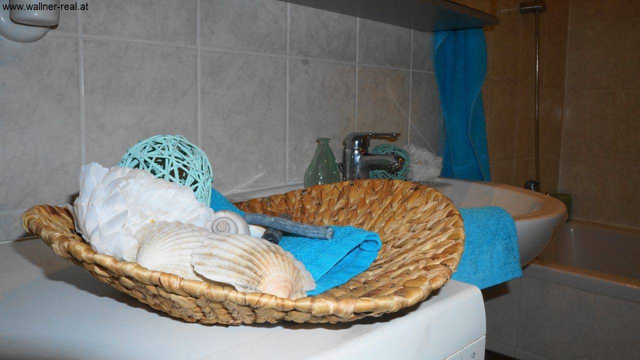 Detailaufnahme der Badezimmerdekoration mit Muscheln und blauen Handtüchern.