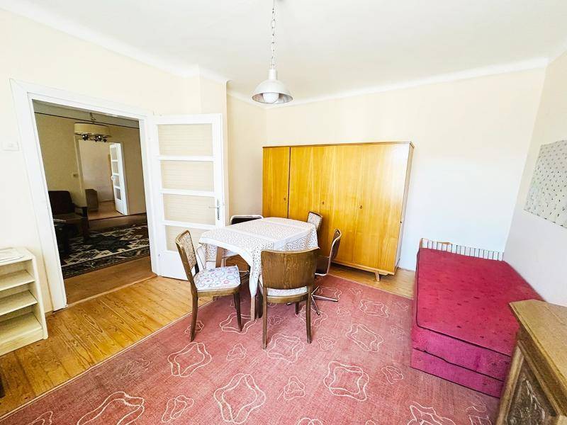 Multifunktionaler Raum mit Esstisch, Bett und Holzschrank, verbunden durch eine Tür.