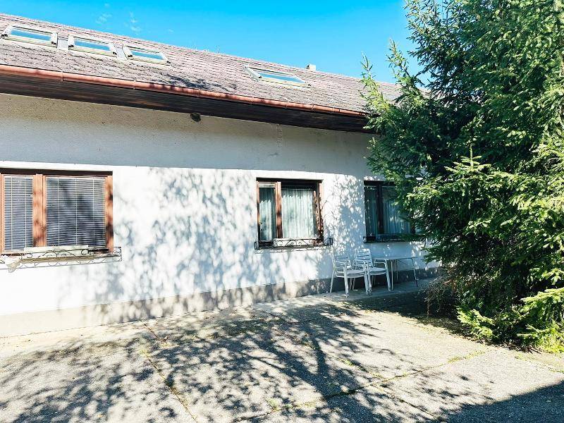 Gebäudeseite mit Fenstern, Jalousien und einer kleinen Sitzgelegenheit im Freien.