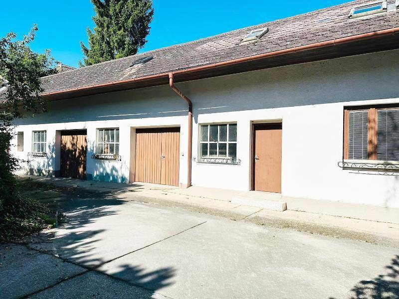 Rückseite eines Gebäudes mit mehreren Türen, Fenstern und einem gepflasterten Bereich.