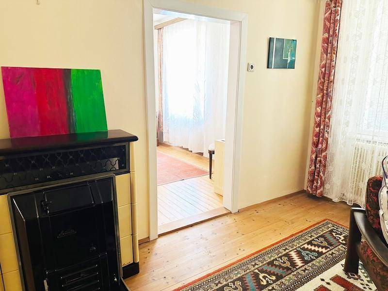 Gemütliches Wohnzimmer mit Holzboden, Teppich und einem traditionellen Kachelofen.