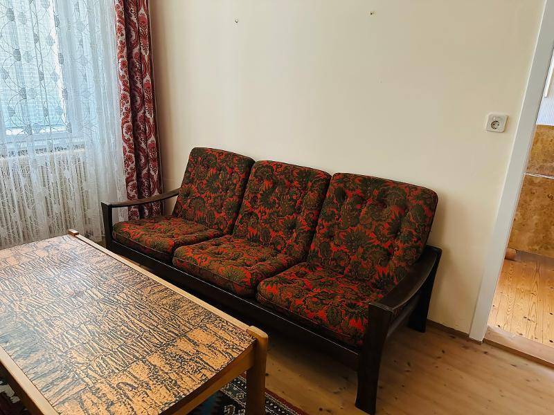 Wohnzimmer mit einem floral gemusterten Sofa und einem Holztisch, beleuchtet durch ein Fenster.