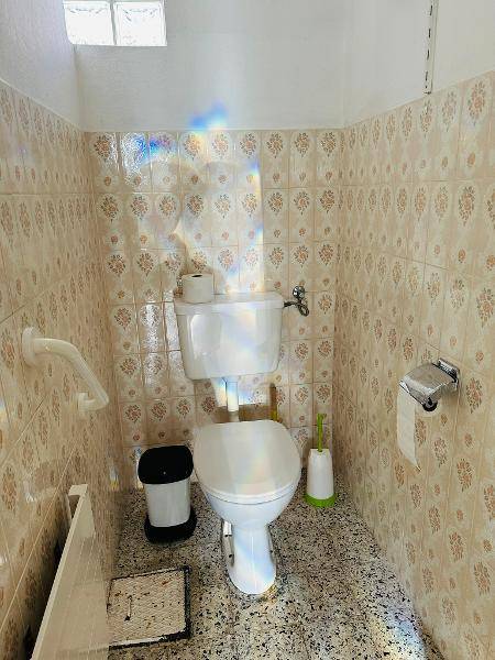 Separate Toilette mit WC, Haltegriff und gemusterten Fliesen an den Wänden.