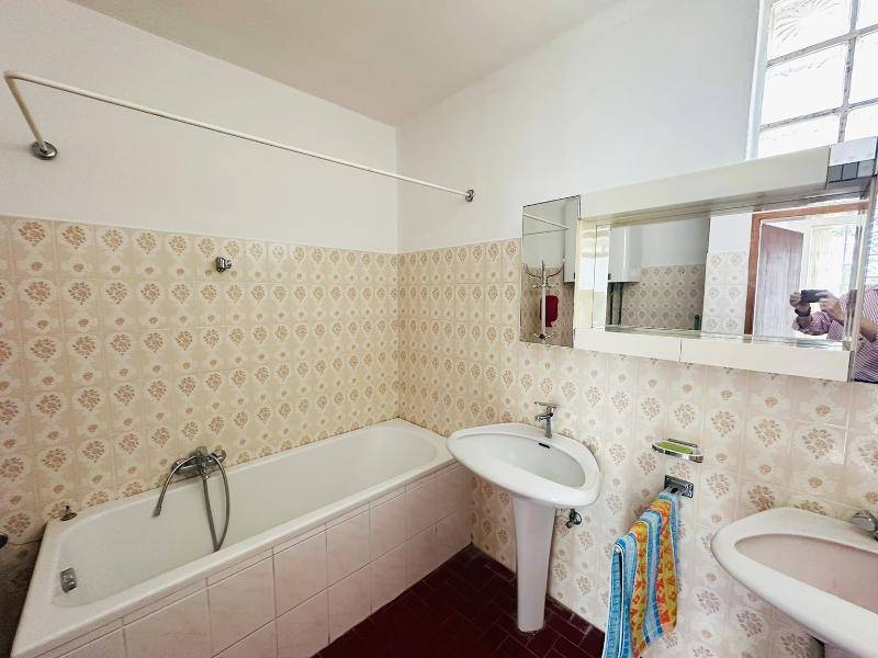 Badezimmer mit Badewanne, Waschbecken und Spiegelschrank, ausgestattet mit gemusterten Fliesen.