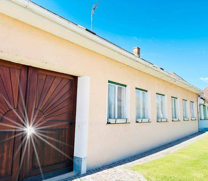 Helle Fassade eines Gebäudes mit mehreren Fenstern und einem gepflegten Rasen unter blauem Himmel.