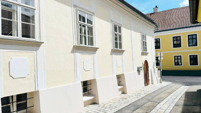 Seitenansicht eines historischen Gebäudes mit heller Fassade und gepflasterter Gasse.