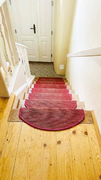 Holztreppe mit roten Teppichstufen und weißem Geländer, führt in den oberen Bereich.