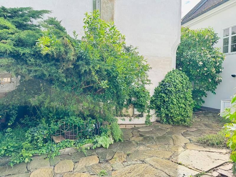 Steinplattenweg in einem begrünten Innenhof mit üppiger Vegetation und alten Mauern.