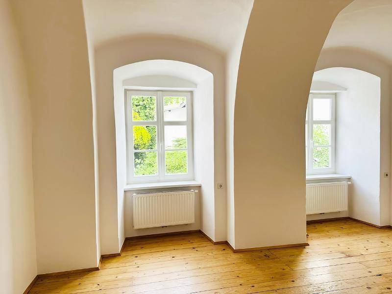Geräumiger Raum mit Holzboden, hohen Gewölbedecken und zwei großen Bogenfenstern.