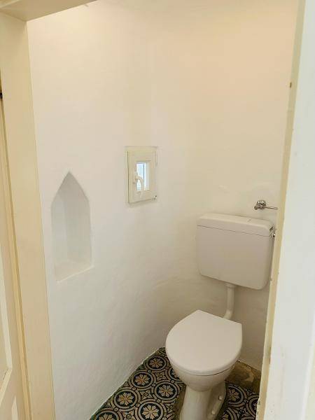 Kleines WC mit weißer Toilette und gemusterten Bodenfliesen in einem schlichten Raum.