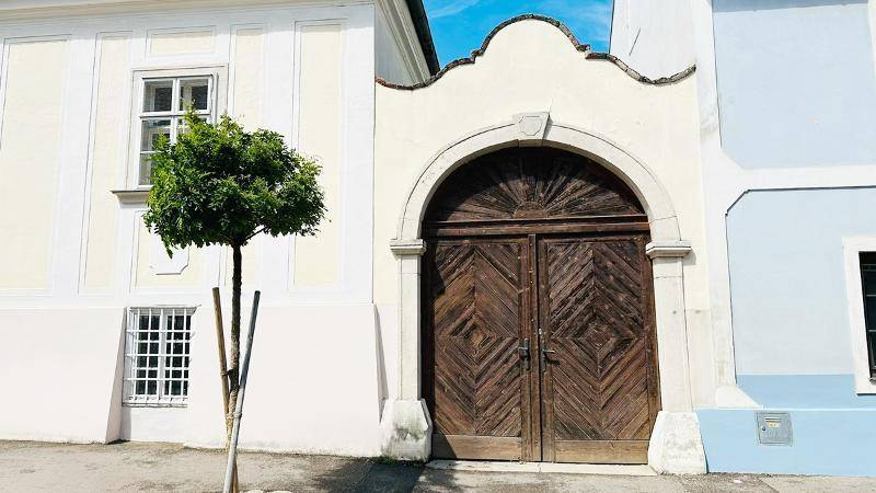 Großes, altes Holztor mit Rundbogen und dekorativer Fassade an einem historischen Gebäude.