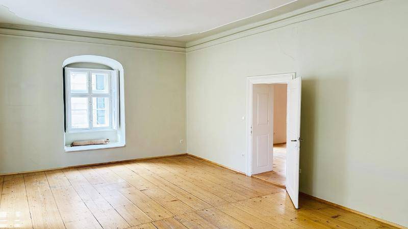 Heller, leerer Raum mit Holzdielenboden, hohen Decken und einem großen Fenster.