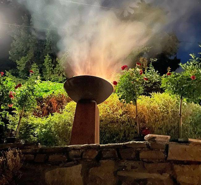Stimmungsvolle Feuerstelle im Garten, umgeben von üppiger Bepflanzung und leuchtenden Blumen.