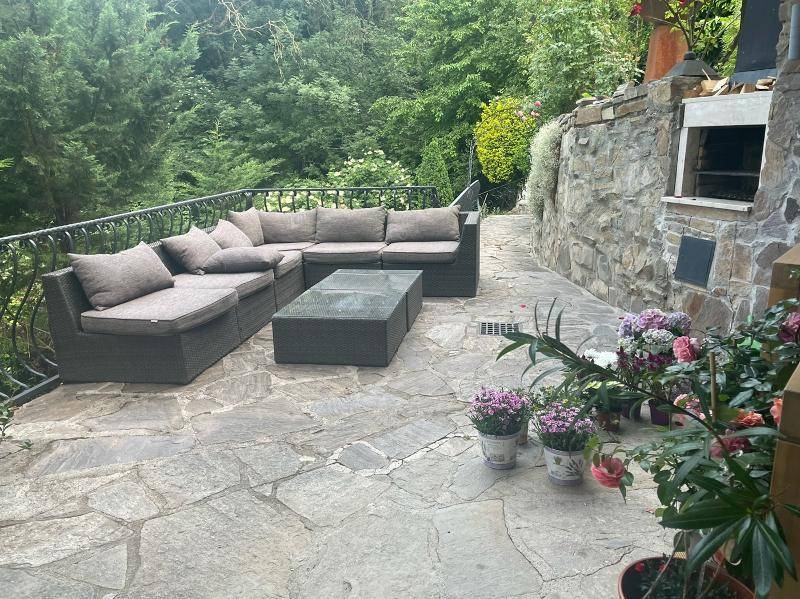 Gemütliche Steinterrasse mit Outdoor-Sofa und Grillbereich, umgeben von üppigem Grün.
