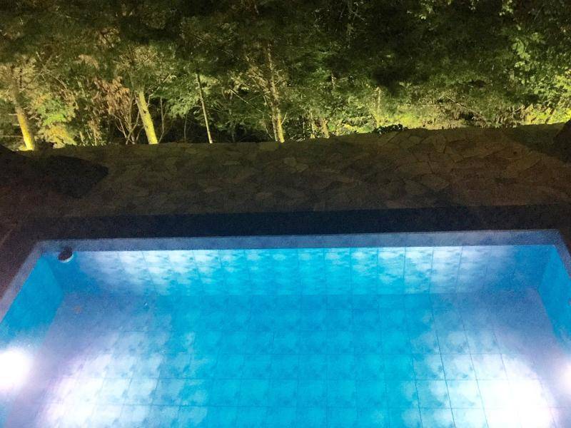 Beleuchteter Außenpool bei Nacht, umgeben von einer Steinmauer und Bäumen.