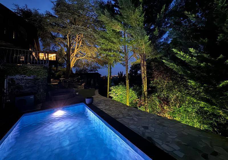 Stimmungsvoll beleuchteter Poolbereich bei Nacht, umgeben von Bäumen und mit Fernblick.