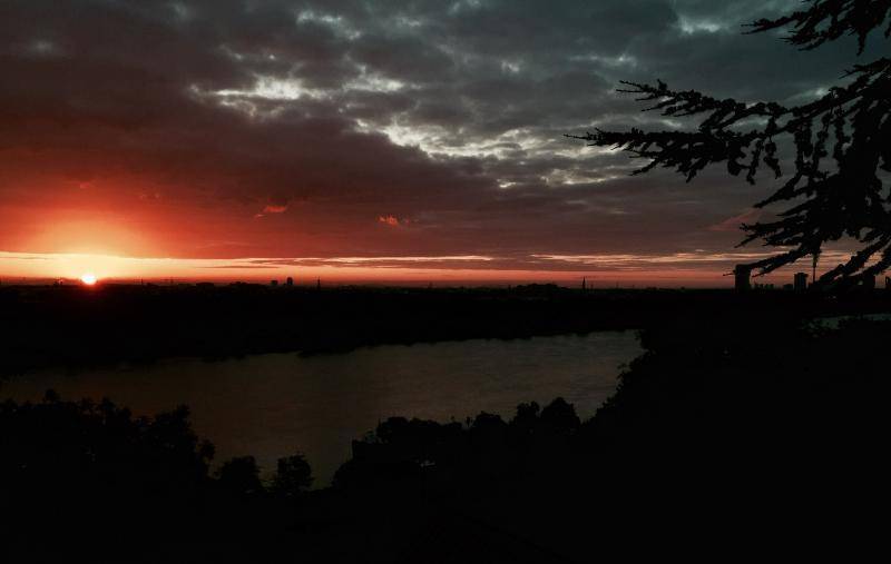 Dramatischer Sonnenuntergang über der Stadt und dem Fluss, mit dunklen Wolken.