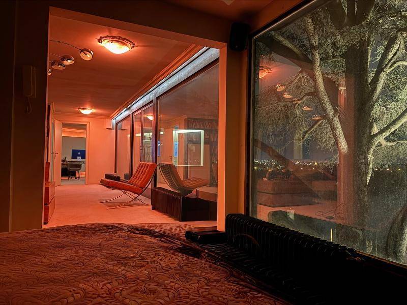 Schlafzimmer mit großen Fenstern, die einen nächtlichen Blick auf die Stadt und die Natur bieten.