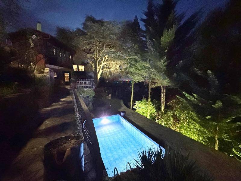 Beleuchteter Außenpool bei Nacht mit einem charmanten Haus im Hintergrund und Fernblick.