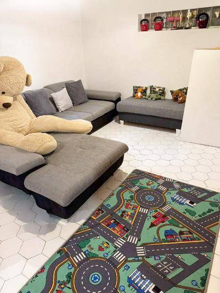 Geräumiger Wohnbereich mit großem Sofa und einem Spielteppich auf sechseckigen Fliesen.