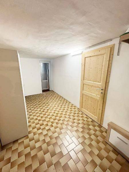 Kellerraum mit gefliestem Boden und einer Holztür, ideal als Abstellraum.