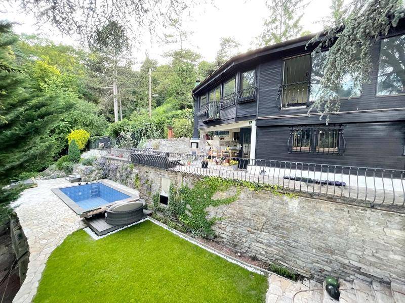 Modernes Haus mit dunkler Holzfassade, großem Garten, Pool, Whirlpool und Terrasse in grüner Natur.