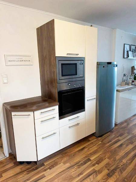 Funktionale Küche mit integriertem Backofen, Mikrowelle und einem freistehenden Kühlschrank.