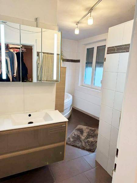 Modernes Badezimmer mit Waschtisch, Spiegelschrank und einem Fenster für natürliche Belüftung.