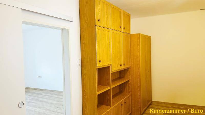 Kinderzimmer oder Büro mit praktischen Einbauschränken aus hellem Holz und Schiebetür.