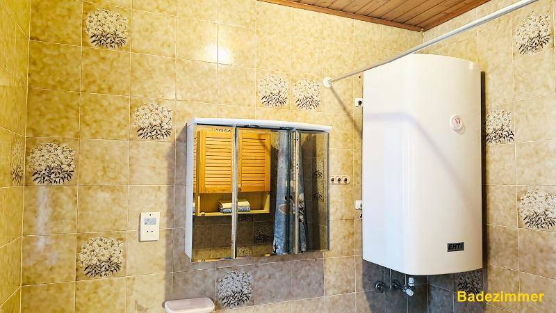 Badezimmer mit Spiegelschrank, Warmwasserboiler und gemusterten Wandfliesen.