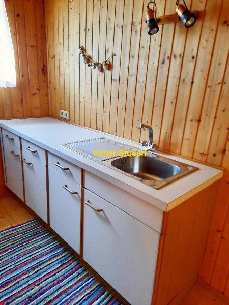 Kleine Küchenzeile mit Spülbecken, Arbeitsplatte und rustikaler Holzvertäfelung an den Wänden.