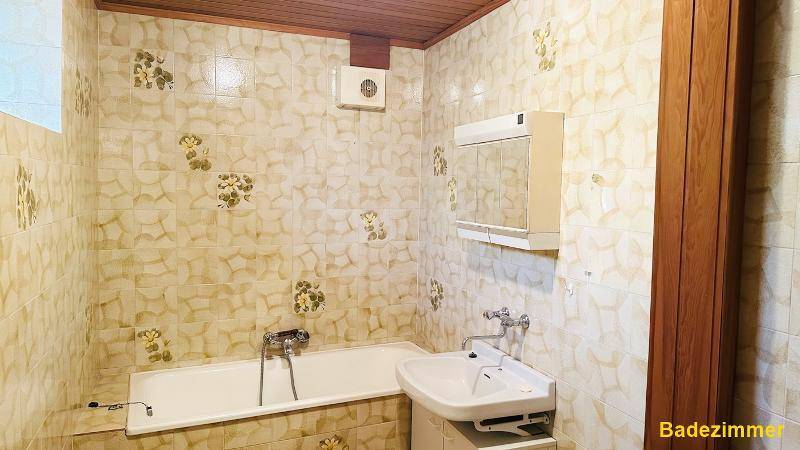 Badezimmer mit Badewanne, Waschbecken und gemusterten Fliesen, ausgestattet mit Holzdecke.