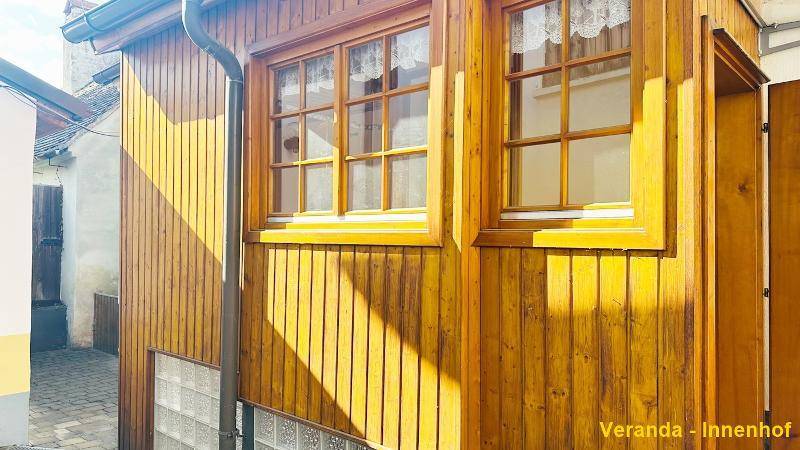 Veranda mit Holzverkleidung und Fenstern, die zum Innenhof ausgerichtet sind.