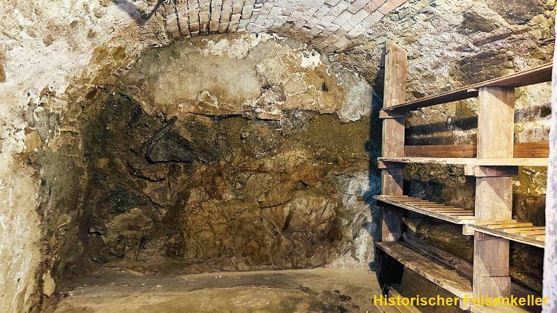 Historischer Felsenkeller mit rustikalen Steinwänden und Holzregalen für Lagerzwecke.