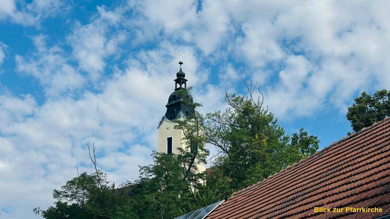 Blick auf einen Kirchturm über den Dächern der umliegenden Häuser unter blauem Himmel.