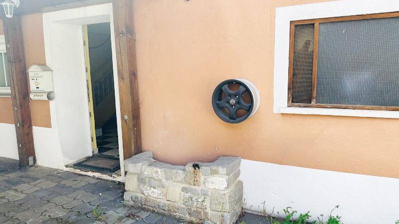 Eingangsbereich mit Briefkasten, dekorativem Rad und Steinbrunnen.