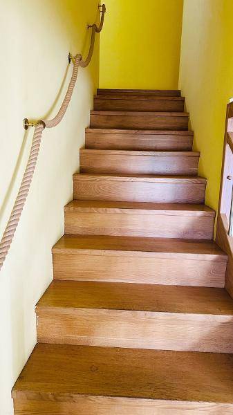 Holztreppe mit Seilgeländer und gelben Wänden, die nach oben führt.