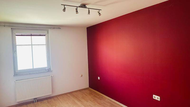 Schlafzimmer mit roter Akzentwand, Holzfußboden und Fenster.