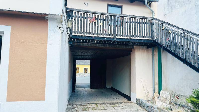Außenansicht eines Gebäudes mit Holztreppe und Durchgang zur Straße.